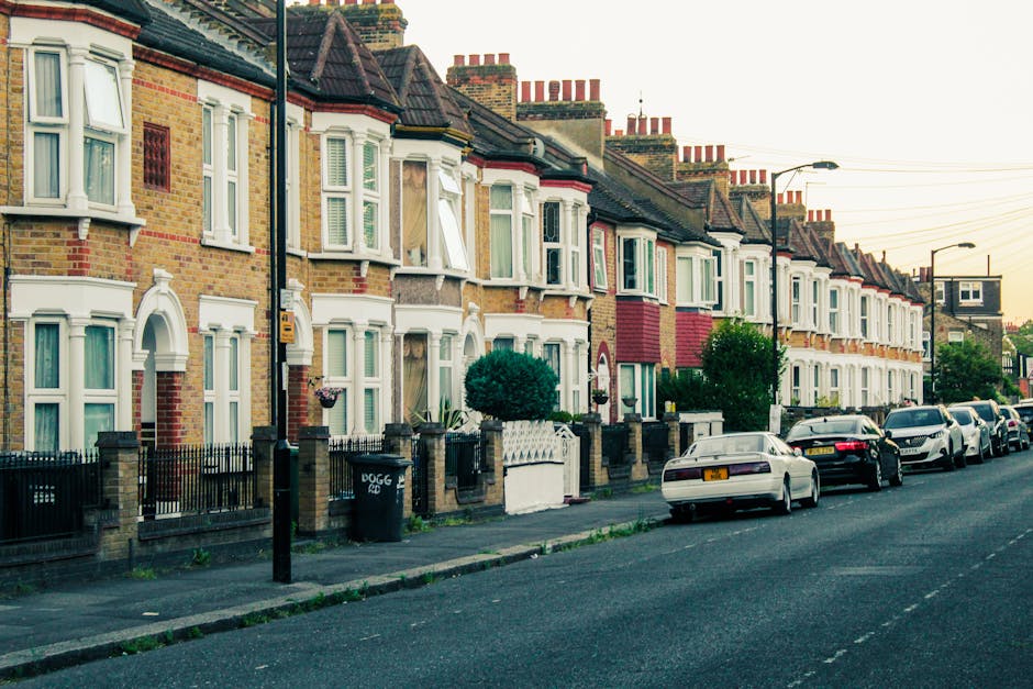 Photograph of a row of terraced houses on a residential street in Highbury during daytime, with brick exteriors and bay windows. Several houses have white window frames and decorative architectural de